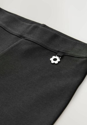 Leggings noirs avec une texture lisse, présentant un accent en métal argenté en forme de fleur contrastante sur la taille.