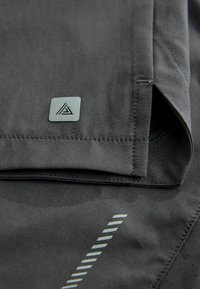 Szare szorty sportowe o eleganckim kroju, z perforowaną teksturą, trójkątną naszywką z logo oraz subtelnym wzorem pasków po bokach.