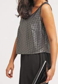 Stříbrná top bez rukávů s pestrobarevnými kuličkami a volným střihem, spárovaná s černou sukní a lesklou černou kabelkou. Hladký materiál s lesklými akcenty.