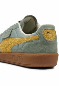 Baskets en suede vert avec une bande texturée jaune, des accents crème, une semelle en caoutchouc et un petit logo au talon. Fermeture à bande Velcro.