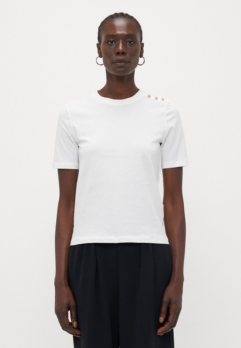 White cotton t-shirt with short sleeves, round neckline, and three decorative gold buttons on the left shoulder. Smooth texture, fitted design.