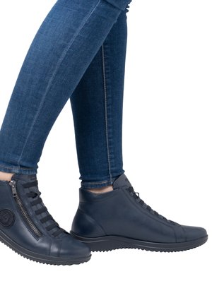 Marineblaues Leder-Ankle-Boot mit glatter Textur, Reißverschluss, Schnürakzenten und robuster Sohle, kombiniert mit blauen Skinny-Jeans.