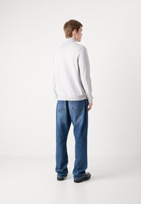 Lys grå langermet topp med ribbet tekstur, kombinert med løstsittende mørkeblå denimjeans med baklommer og synlig søm.