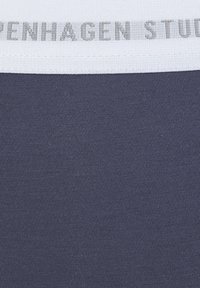 Marineblauwe ribstof met een witte elastische band met de tekst "COPENHAGEN STUDIO" in grijze letters, wat de nadruk legt op een soepele textuur en gestructureerd ontwerp.