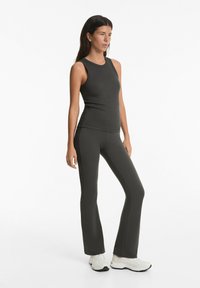 Canotta a coste grigio scuro abbinata a leggings svasati coordinati. Entrambi i capi presentano una texture liscia e cuciture sottili. Scarpe da ginnastica bianche completano l'outfit.