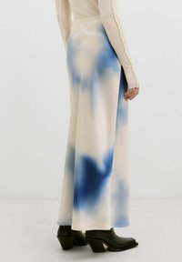 Lange, vloeiende rok in roomwit met blauwe tie-dye patronen. Glad fabric, hoge taille en een zijscheur. Gecombineerd met zwarte, chunky-heeled laarzen.
