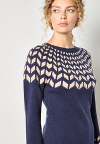 Granatowy sweter dzianinowy z jasnobeżowym geometrycznym wzorem na dekolcie, okrągłym kołnierzykiem, długimi rękawami i miękkim, teksturowanym wykończeniem.