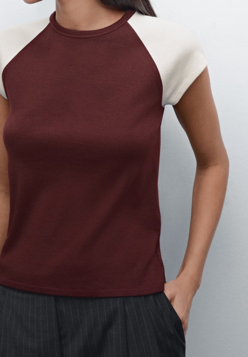 Bordeaux kortærmet t-shirt med cremefarvede raglanærmer. Lavet af glat stof, med en rund halsudskæring og tætsiddende silhuet.