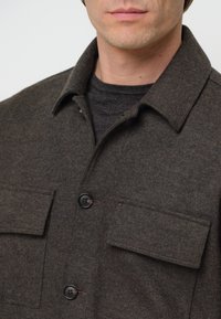 Bruin, gestructureerd wollen shirtjack met een puntige kraag, twee borstzakken en zwarte knopen, met een gelaagd zwart topje eronder.