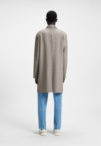 Cappotto lungo a quadri in tessuto beige, con colletto a punta. Abbinato a pantaloni azzurri chiari e sneakers bianche.