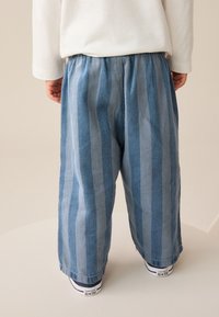 Ljusblå randiga byxor i denim; vida ben, elastisk midja och uppvikta fållar. Matchade med vita sneakers.