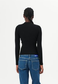 Top nero a costine con maniche lunghe, forma aderente e collo alto, abbinato a jeans blu a vita alta con doppie tasche posteriori.