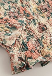 Nahaufnahme von elastischem Stoff mit Raffung und Blumenmuster in zurückhaltenden Rosa-, Grün- und Cremetönen.