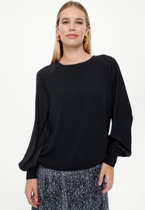 Blusa nera a maniche lunghe con scollo rotondo e maniche arricciate. Il tessuto è morbido con una vestibilità comoda, abbinata a una gonna a fantasia.