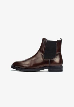 Bottines Chelsea en cuir marron avec panneaux élastiques sur les côtés et une languette de boucle. Texture lisse, bout rond et semelle en caoutchouc.