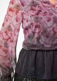 Durchsichtige Bluse mit floralem Rosenmuster in rosa und lila Tönen, kombiniert mit einem dunklen, plissierten unteren Teil und Paillettenakzenten.