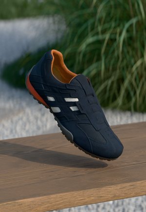 Pantof de sport navy cu un superior din plasă, interior portocaliu și talpă din cauciuc gri. Are dungi decorative albe pe laturi.
