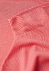 Gros plan sur un tissu côtelé rose corail avec une petite pièce rectangulaire cousue, montrant les détails de texture et de couture.