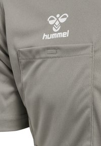 Grå Hummel kortærmet skjorte med en forlommes og et hvidt logo. Stoffet ser glat og struktureret ud.