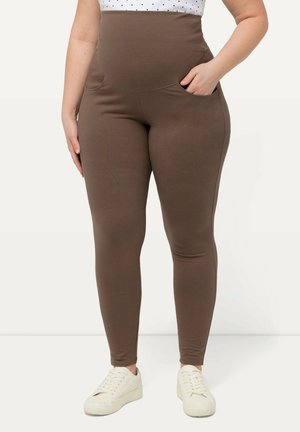 Brown high-waisted leggings with a smooth texture, featuring side pockets and a fitted design, paired with white sneakers.