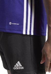 Paarse sportshirt met witte zijstrepen, met het "AEROREADY"-logo. Zwarte shorts met het witte "adidas"-logo op het onderbeen.
