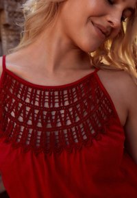 Haut sans manches rouge avec un col en dentelle et un tissu texturé offrant une coupe décontractée, mettant en valeur des détails de couture complexes.