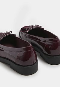 Bordeauxlackskor med rund tå, svart gummisula och dekorativ rosett framtill. Slät yta och blank yta.