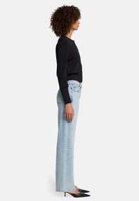 Maglione nero in maglia, jeans a vita alta blu chiaro e décolleté neri con punta. Presenta maniche aderenti e gamba dei pantaloni leggermente svasata.