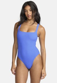 Geribbelde eenpiece badpak in felblauw, met een vierkante halslijn en brede schouderbanden. De stof heeft een zachte textuur en hoge beenuitsnijdingen.