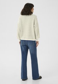 Pulover crem cu textură ușoară și dungi verzi, asociat cu blugi denim largi, de culoare albastră. Ținuta are un fit lejer, casual și manșete dublate.