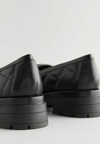 Scarpe in pelle nera con un motivo trapuntato, punta tondeggiante e suola in gomma spessa con scanalature orizzontali. Finitura superficiale testurizzata.