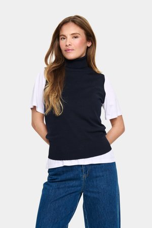 Marinblå mock turtleneck-tröja lager på en vit t-shirt med kort ärm, tillsammans med blå jeans. Mjukt stickat material med ribbade avslut.