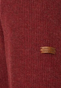 Rippstrick-Pullover aus tiefrotem Stoff mit strukturiertem Finish und einem braunen Lederetikett, auf dem "Authentic Clothing Redmond" geprägt ist.