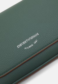 Zelená texturovaná kožená peněženka s hnědým lemem, s embosovaným logem "EMPORIO ARMANI MILANO 1981" ve stříbrné barvě. Obdélníkový tvar, elegantní design.