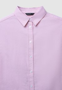 Helles rosa Hemd mit Knopfleiste und klassischem Kragen, das eine glatte Textur aufweist und sechs weiße Knöpfe entlang der Vorderseite hat. Markenlabel: Calliope.