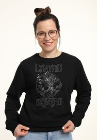Svart sweatshirt med grafisk design som föreställer en örn och en gitarr. Ribbad manschett och halsringning, tillverkad av bomullsblandat tyg.