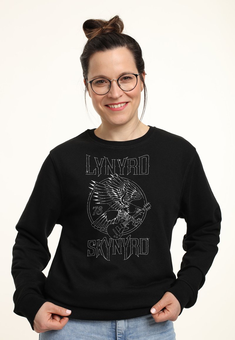 Svart sweatshirt med grafisk design som föreställer en örn och en gitarr. Ribbad manschett och halsringning, tillverkad av bomullsblandat tyg.