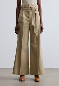 Pantaloni bej cu picior larg și talie înaltă, având o curea texturată, buzunare laterale și un material neted din bumbac.