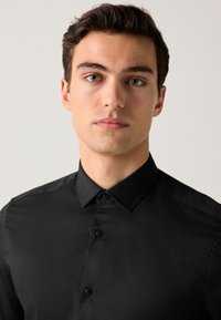 Camicia nera con bottoni e colletto classico, realizzata in tessuto liscio, con una trama sottile e due bottoni neri sul davanti.