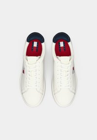 Pair of white lace-up sneakers with red insoles and navy collar, featuring Tommy Jeans logo on the side and insole.