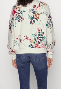 Blommig sweatshirt i krämvit, med färgglada blommor och grönska. Ribbad mudd och nederkant. Matchas med mörkblå jeans.