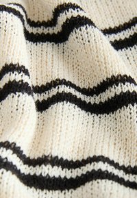 Tissu tricoté couleur crème avec des côtes texturées et des rayures ondulées noires horizontales, présenté en gros plan avec des plis doux.