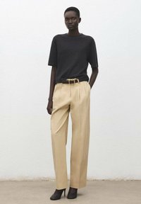 Czarna bluzka z krótkim rękawem w połączeniu z beżowymi spodniami o wysokim stanie. Stylizację dopełnia brązowy pasek i czarne szpilki.