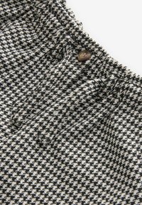 Sort-hvidt houndstooth-mønstret stof med rynkede detaljer i taljen og en brun knaplukning.