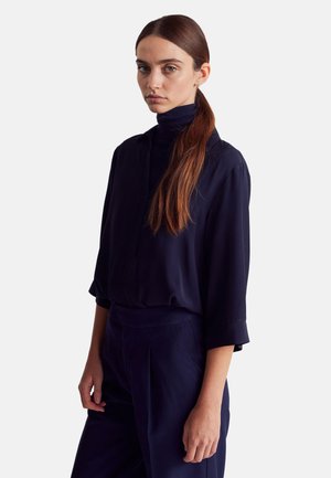 Blusa blu navy con collo alto e maniche lunghe, caratterizzata da una vestibilità comoda e da una texture liscia, abbinata a pantaloni a vita alta coordinati.
