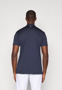 Granatowa koszulka polo z krótkim rękawem, z kołnierzykiem, gładka tekstura, bez widocznych wzorów, jednolity design z tyłu i dyskretnym logo blisko kołnierzyka.