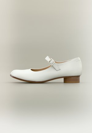 Zapato Mary Jane de cuero blanco con tacón bajo de madera y correa con hebilla plateada, visto desde el lado exterior sobre un fondo neutro.