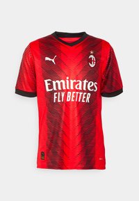 Maglietta rossa da calcio con strisce orizzontali nere, scollatura a V e maniche corte. Presenta un logo sul petto e il testo "Emirates FLY BETTER".