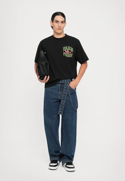 Black t-shirt with green and red "FARM FRESH" text, paired with loose blue denim jeans featuring a decorative strap and silver hardware accents.