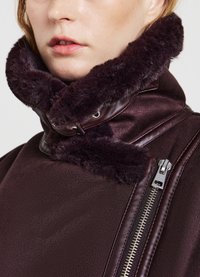 Giacca bordeaux con colletto in pelliccia morbida, zip laterale e superficie liscia. Hardware notevole include una zip argentata.